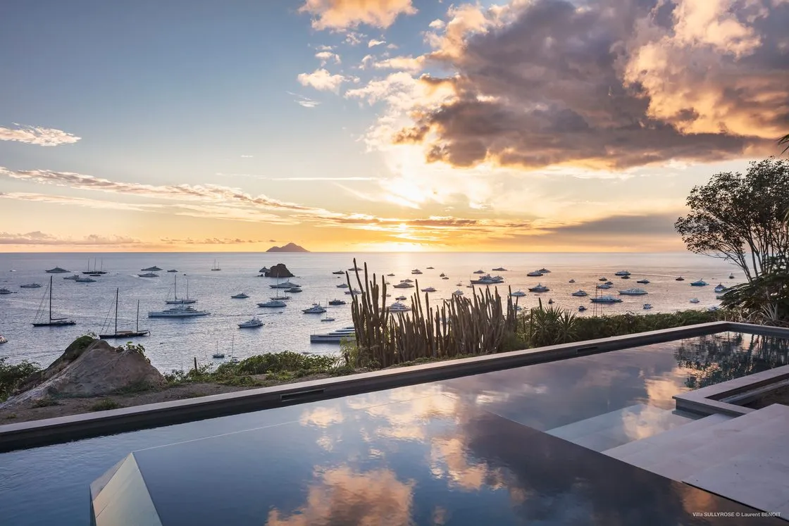 Infinity pool of a Saint-Barthélemy villa at sunset, the bay and sailing boats below