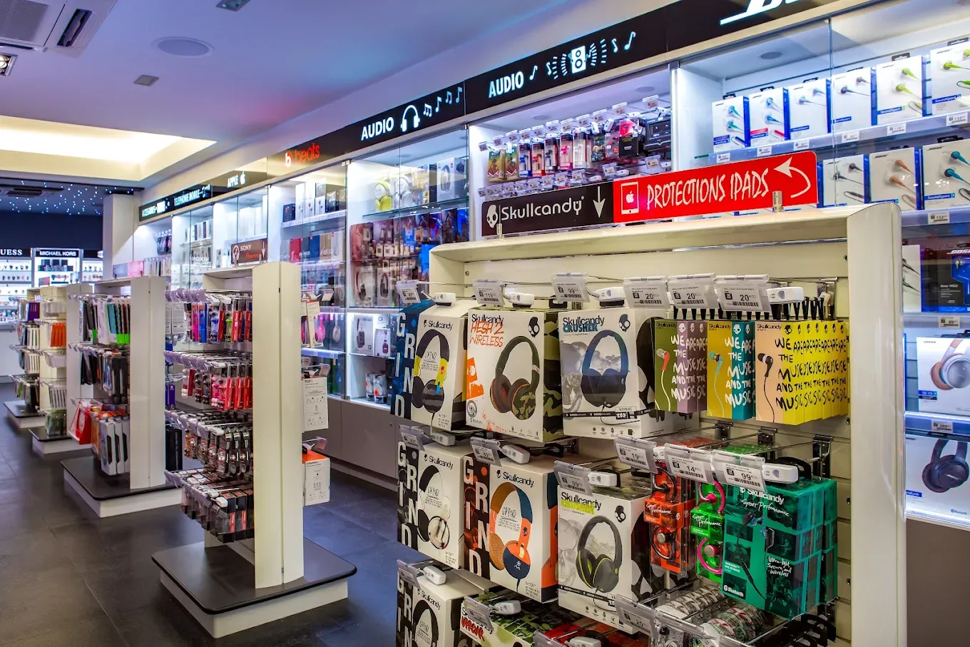 Allées d’accessoires : coques, câbles, casques et protections, sur des présentoirs éclairés.