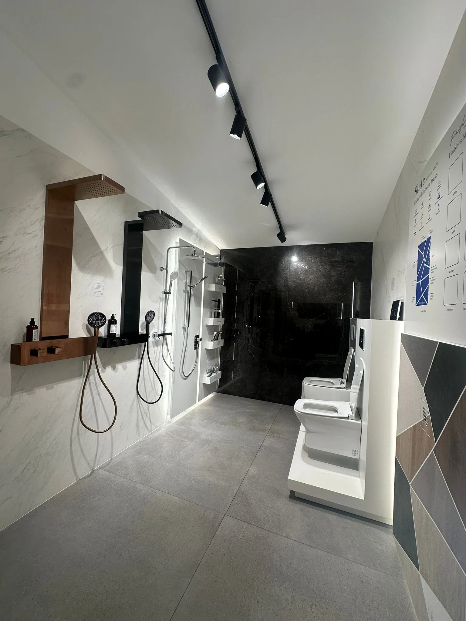 Bathroom display: copper and black shower columns on white marble, dark marble backdrop, wall-hung sanitaryware and a board of finishes.