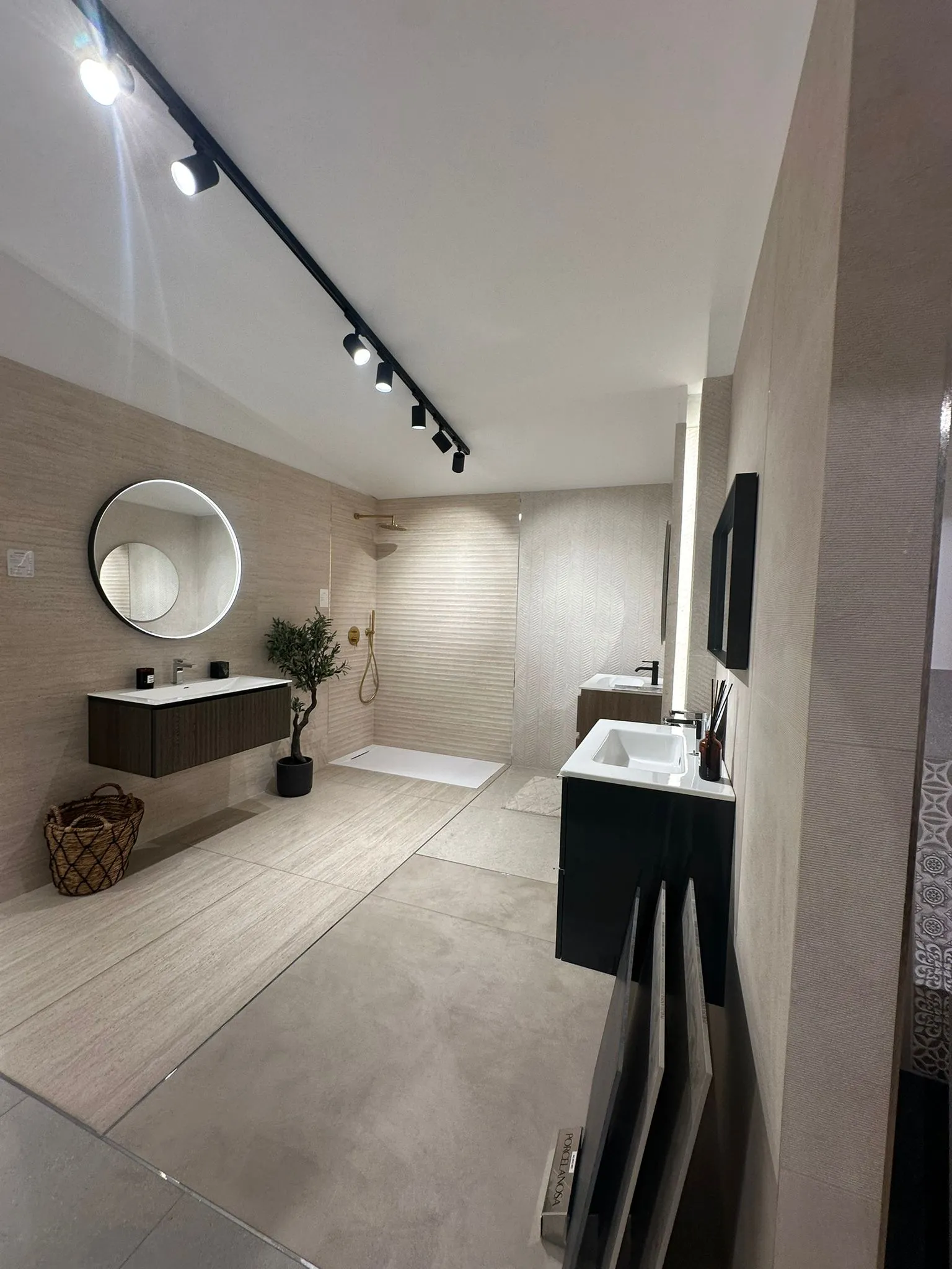 Overall view of the travertine bathroom: two vanity units, a walk-in shower at the back and a wicker basket in the foreground.