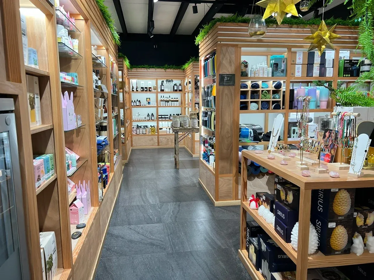 Allée d’art de vivre : étagères de vaisselle, de bougies et d’accessoires de maison, sous une charpente en bois.