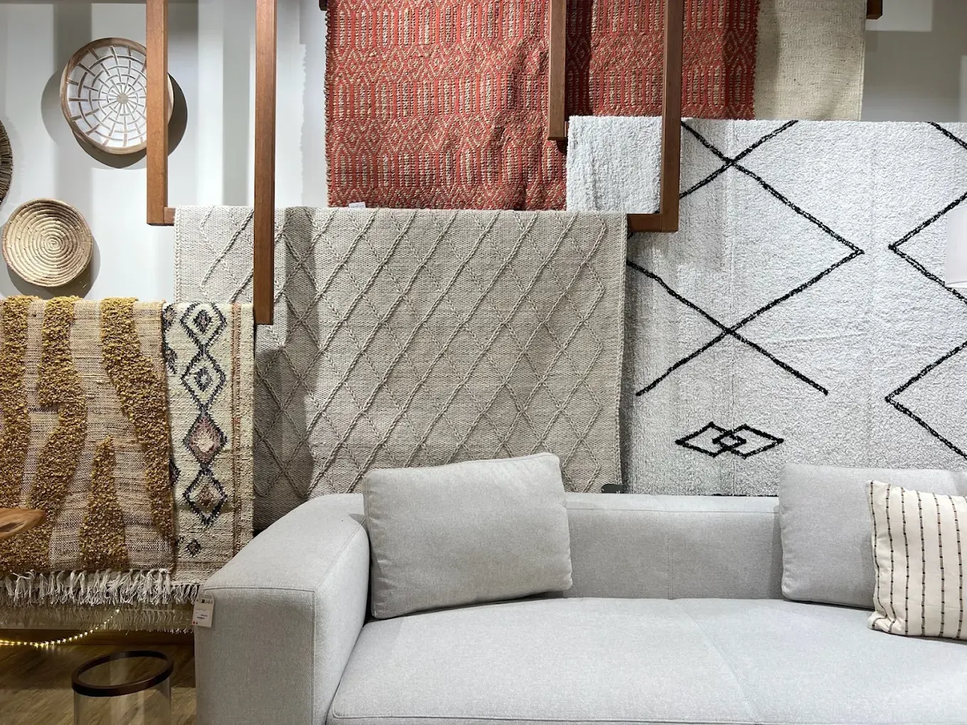 Mur de textiles : tapis berbères, plaids terracotta, paniers tressés et coussins, devant un canapé clair.